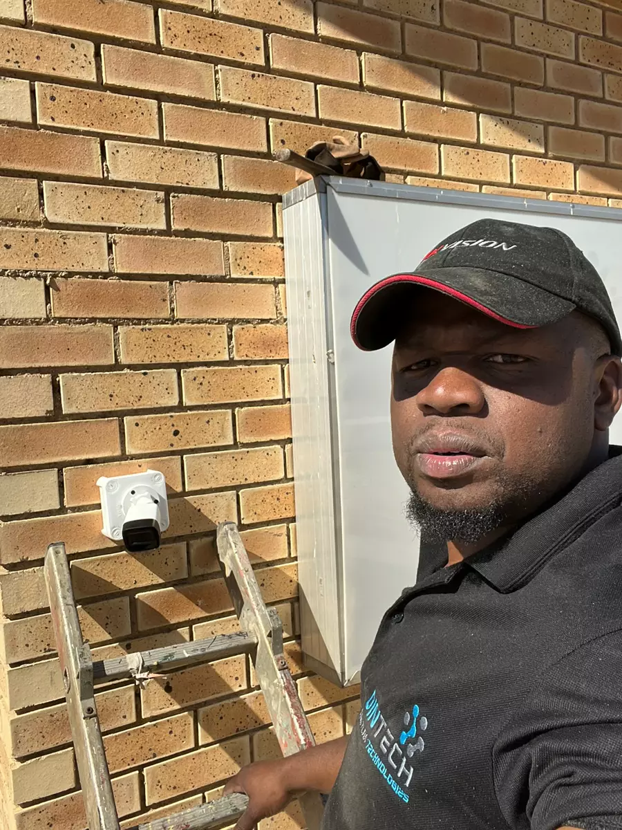 A technician standing beside a brick wall with a newly installed security camera