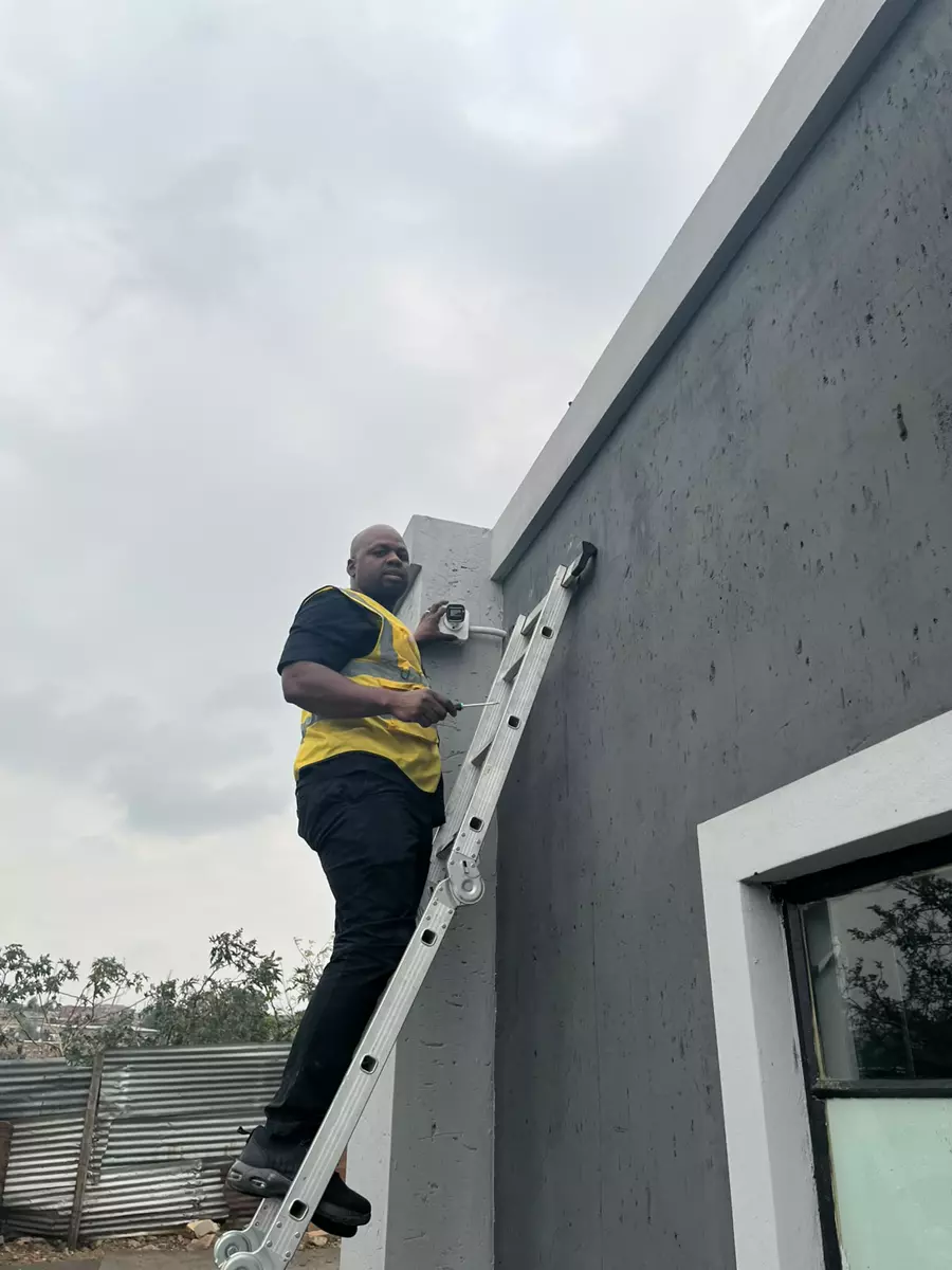 A technician installing a security camera on an exterior wall