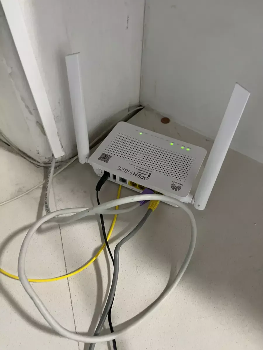 White Huawei router on the floor with cables plugged in