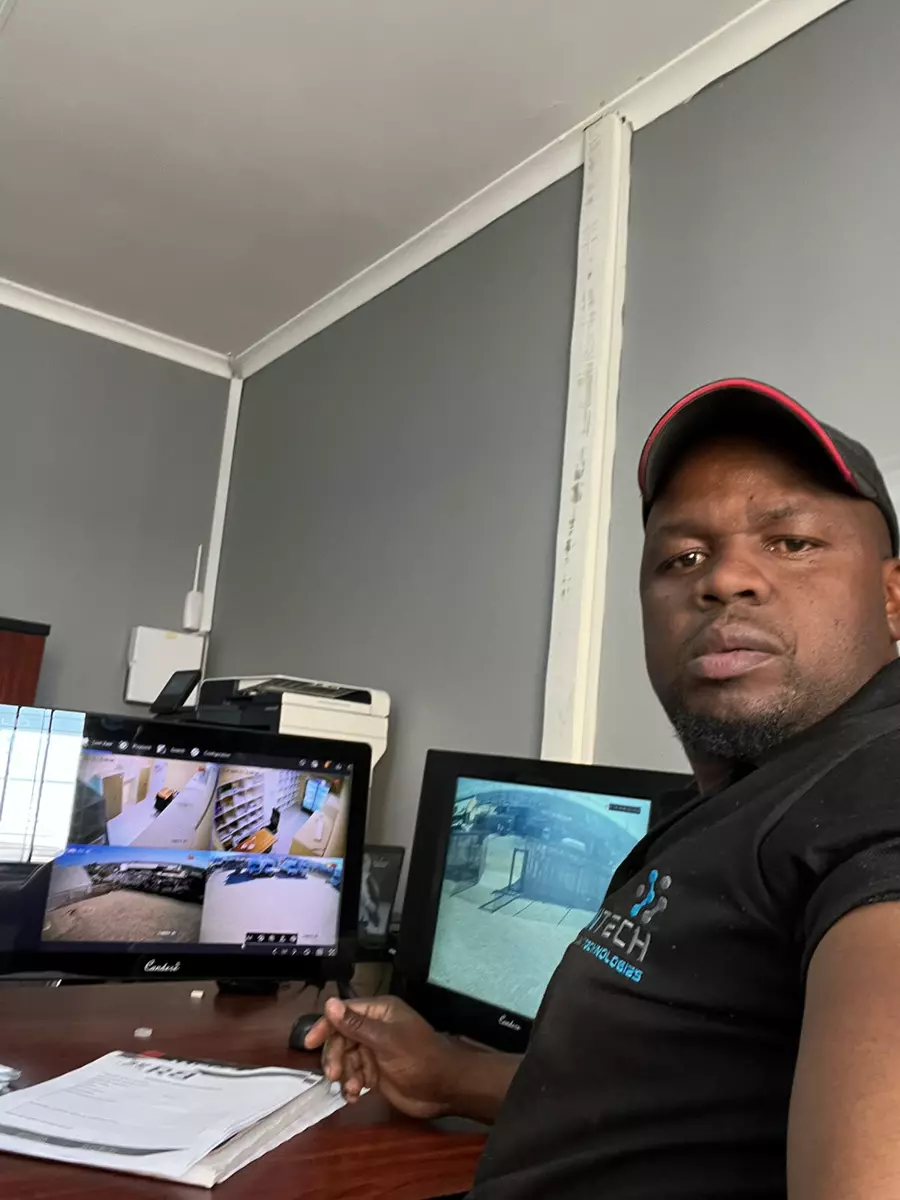 A technician sitting at a desk with security camera monitors and paperwork